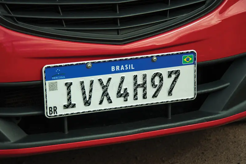 Placa Mercosul brasileira no para-choque de um carro vermelho, em close.